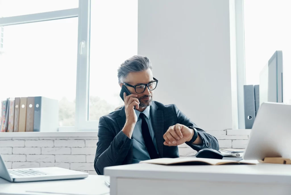 Man checking the time while talking on phone during real estate cold calling