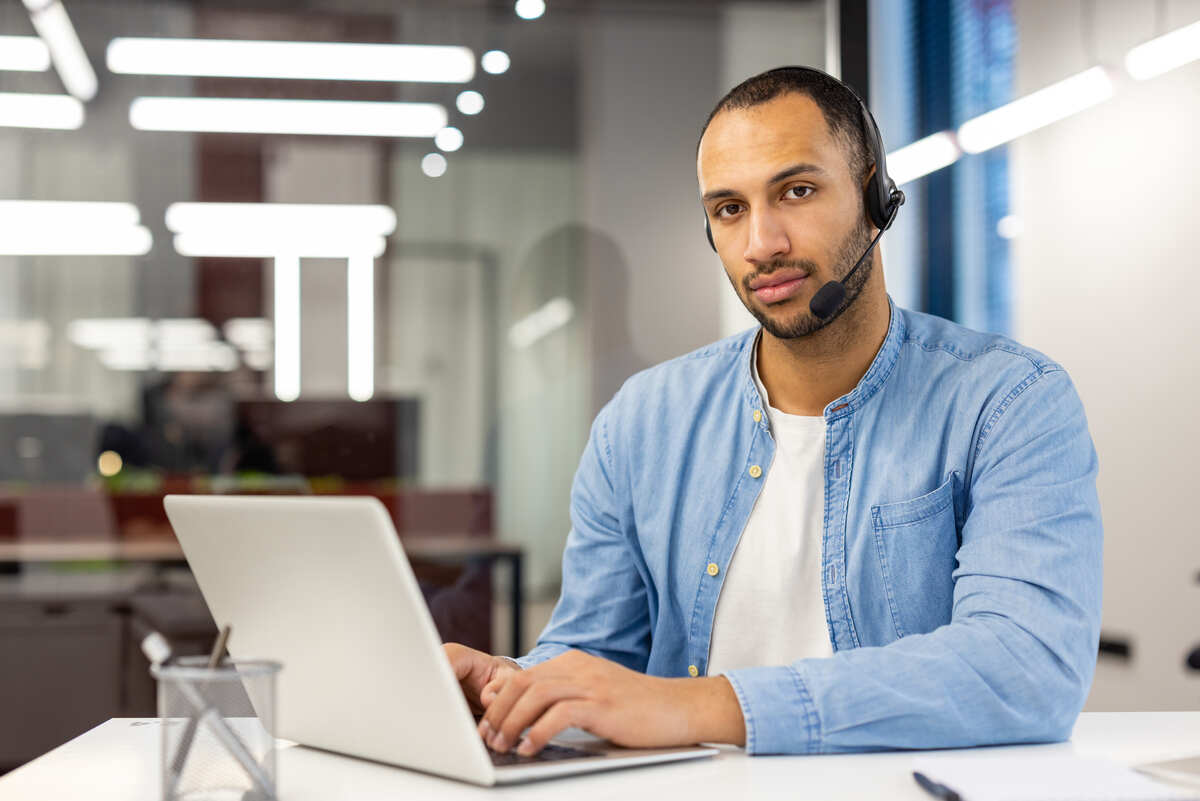 Portrait of a serious hispanic man in a shirt sitting in the office, at the table in front of the laptop and confidently looking at the camera..