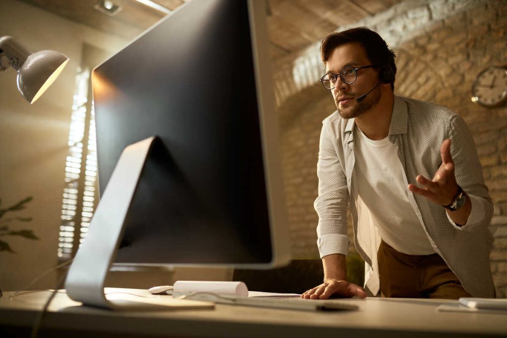 Low angle view of young entrepreneur discussing with someone while making video call over desktop PC from his office.