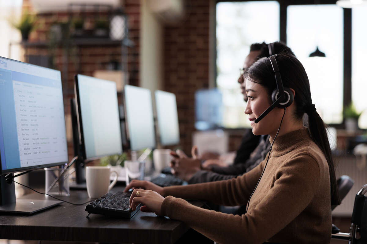 Paralyzed asian employee working at call center reception in disability friendly office. Female operator wheelchair user with impairment giving assistance on customer service helpline.