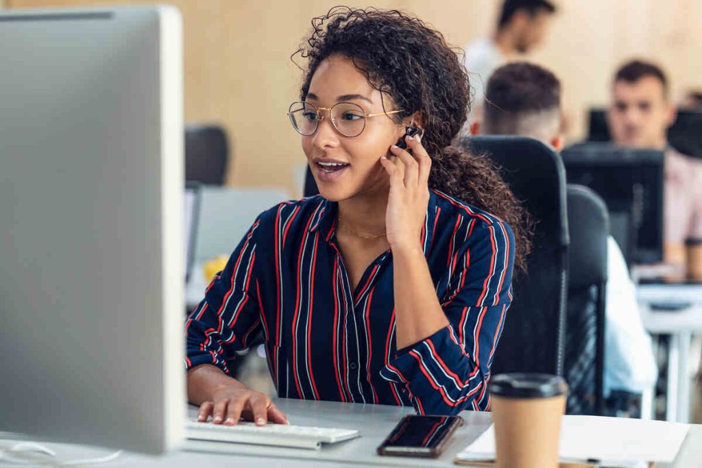 young business woman working with laptop while talking with earphone sitting in a coworking place.