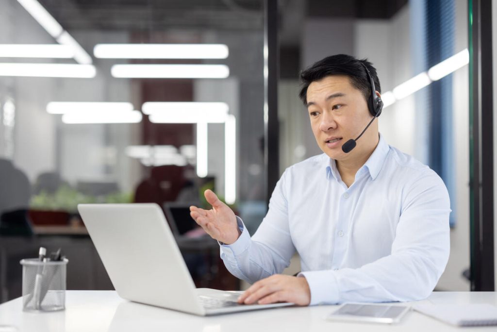 A business professional engages in a discussion during a video call in a well-lit contemporary office setting.